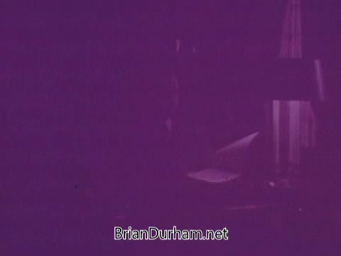 The still appears to be a dimly lit scene from a 1967 Colgate commercial, characterized by a muted color palette with purple tones. The focus is likely on a product or a scenario promoting Colgate, although specific details are obscured by lighting. The atmosphere suggests a cozy or intimate setting, possibly aimed at conveying a sense of comfort or reliability associated with the brand.