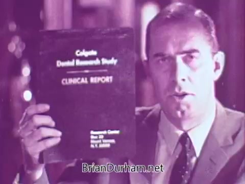 The still features a man in a suit holding up a publication titled 'Colgate Dental Research Study: Clinical Report.' He appears to be making a presentation or endorsement, emphasizing the significance of the study in relation to Colgate products. The overall tone is authoritative and informative, typical of advertising from that era.
