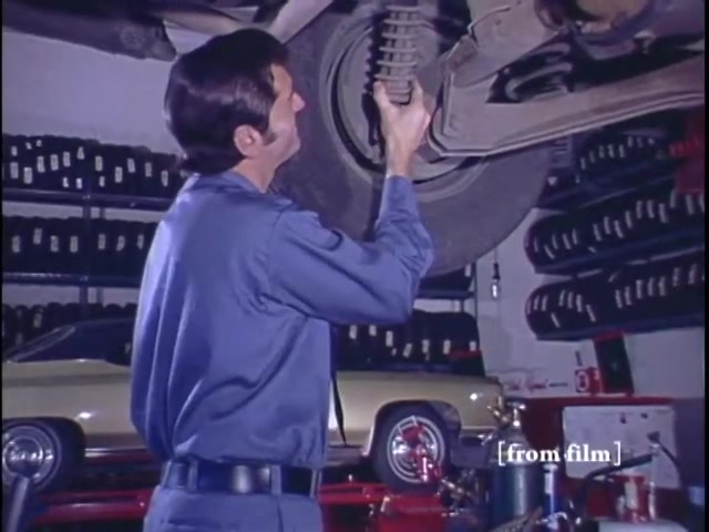 The still from the 'Nichols Automotive' commercial features a mechanic in blue work attire, inspecting a vehicle's suspension system from underneath. The setting appears to be an automotive shop, with various tools and parts visible in the background, highlighting the commercial's focus on car maintenance and service. The commercial concludes with the logo for 'Nichols Discount Center,' indicating the promotional nature of the advertisement. The lab paperwork dates the film to 1971, utilizing Ektachrome positive film for a vibrant appearance.