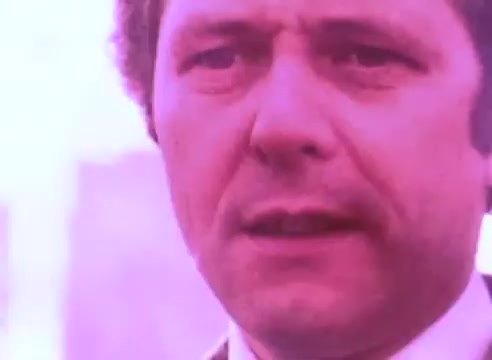 The still features a close-up of a man with a serious expression, set against a softly blurred background. The overall color tone is a muted pink. The man's face suggests a tone of concern or intensity, possibly addressing issues related to ex-offenders. The visual style appears to be typical of a public service announcement, focusing on conveying an important message.