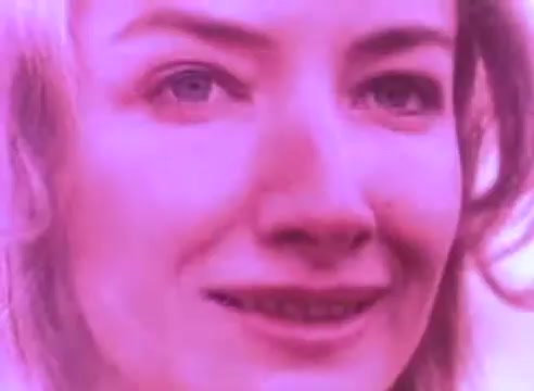 The still features a close-up of a woman's face with a soft, pink hue, giving it an ethereal quality. Her expression is subtle yet inviting, suggesting openness or vulnerability. The focus on her features conveys an emotional connection, likely relating to the themes of reintegration and understanding presented in the PSA.