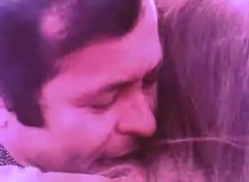 The still from 'PSA - Ex Offender 2' features a man and a woman in a close embrace, conveying a sense of intimacy and emotional connection. The man's expression appears thoughtful or solemn, while the woman's hair partially obscures her face, suggesting vulnerability. The color of the image has a pinkish hue, which contributes to the emotional tone of the scene. Overall, the image emphasizes themes of support and understanding in the context of reentry and rehabilitation.