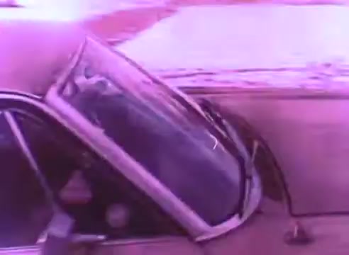 The still from 'PSA - Ex Offender 2' features a close-up of the side of a car, with the window partially rolled down. The image is tinted with a purplish hue, creating a stylized atmosphere. The background appears to show snow, suggesting a cold environment. The scene likely aims to evoke feelings related to the themes of the PSA, focusing on the experiences of ex-offenders.