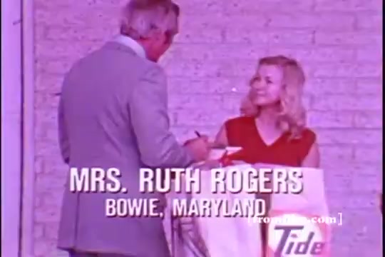The still features a man in a light suit interacting with a smiling woman, identified as Mrs. Ruth Rogers from Bowie, Maryland. The scene is likely set in a domestic or community context, reflecting a friendly atmosphere. The Tide logo is visible, indicating it's a commercial for the laundry detergent. The colors are typical of 1970s aesthetics, with a slightly faded vintage look.