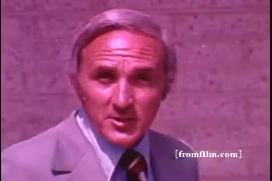 The still features a man in a light-colored suit with a patterned tie, likely presenting a commercial for Tide. He has a serious expression, engaging directly with the camera against a textured background. The overall color tone is warm, typical of 1970s film aesthetics.