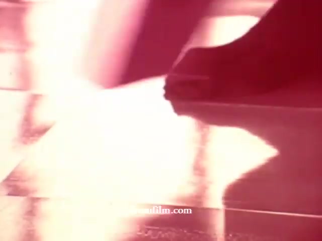 The still from the 16mm film features a close-up of a foot, possibly in the act of cleaning, on a shimmering floor. The lighting creates a warm, radiant glow, emphasizing the reflective surface beneath. The colors appear slightly overexposed, lending a vintage feel, typical of older cleaning product commercials. This scene likely captures the essence of cleanliness and effectiveness, aligning with the themes of Glamolene, Liquid Glory, and Spray-n-Vac showcased in the collection.