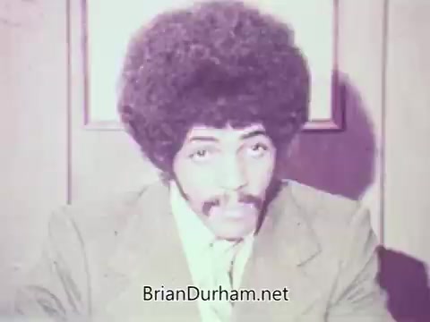 The 16mm still from 'Newsfilm: 'Fight against Record Piracy'' from Stax Records in 1971 features a well-dressed individual with a prominent afro, addressing the issue of bootleg recordings. Rather than focusing on cassette tape copying, the film highlights the unauthorized production and distribution of artists' music. This reflects the music industry's growing concern over illegal practices impacting artists and labels during that era. The context emphasizes the need for protection of intellectual property rights in the music business.