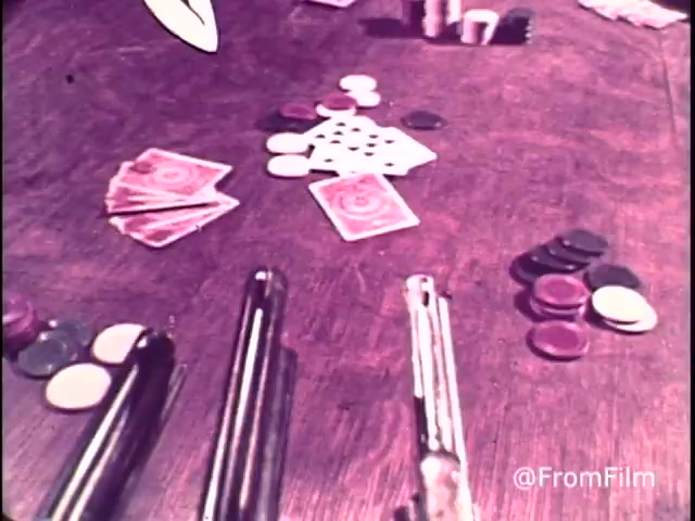 The still from the 1970s M&M's 'Go Fish' commercial features a tabletop scene with playing cards, chips, and a pair of toy guns, highlighting a playful, card-game setting. The presence of red candies emphasizes the era, as red M&M's were available before being replaced by orange in 1976. The tagline 'For good, clean fun every time - M&M's chocolate candies: plain and peanut' complements the lighthearted theme of the commercial.