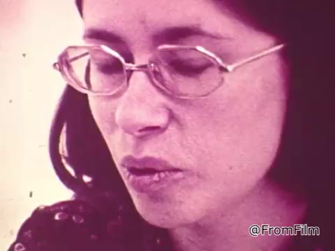 The still features a woman with glasses, focused as she engages in conversation about the TouchTone phone. The background suggests a typical 1970s setting, potentially highlighting the simplicity and user-friendly nature of TouchTone technology compared to traditional rotary phones. The image captures a contemplative moment, likely emphasizing the benefits and ease of use of the newer phone system.