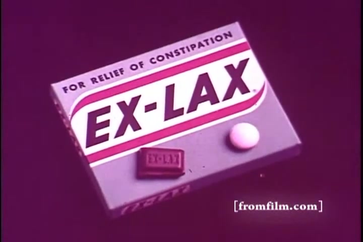 The still features a close-up of an Ex-Lax laxative package from the 1970s. The box is prominently labeled 'EX-LAX' with the tagline 'FOR RELIEF OF CONSTIPATION.' Next to the box are two tablets: one brown and rectangular, and one round and white. The background is a solid, vibrant color, likely purplish, emphasizing the product.