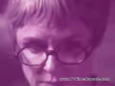 The still appears to feature a close-up of an older woman with short hair and glasses. The image has a purple tint, giving it a vintage or stylized effect. The expression on her face suggests concentration or contemplation, likely in the context of a commercial for Scott Towels.