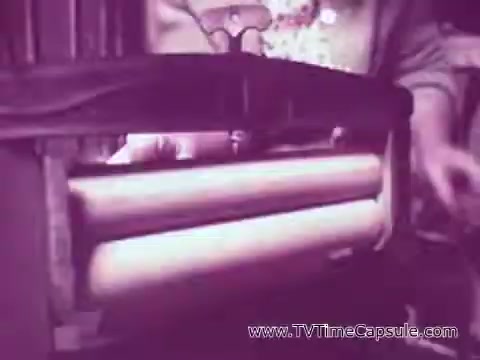 The still shows a close-up of a machine or device with two white rolls, likely depicting the dispensing mechanism of Scott Towels. The surrounding area appears to be dimly lit, creating a vintage atmosphere typical of older commercials. The focus is on the functional aspect of the product, suggesting usability in everyday life.