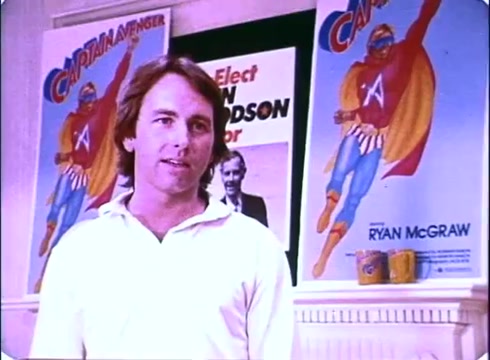 The still from 'Hero at Large' features John Ritter in a casual white shirt, standing in front of vibrant posters depicting a superhero named 'Captain Avenger.' The background suggests a campaign setting with the text 'Elect' and a photo of a candidate, likely connected to the film's plot. The overall mood is lighthearted and comedic, typical of the film's premise. The image captures the essence of the 1980s style, reflecting the playful tone of the movie.
