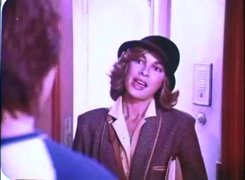 The still from the 'Hero at Large' movie promos features a young woman in a stylish hat and a tailored jacket, appearing to engage in conversation as she stands in a doorway. The scene captures a moment of intrigue or interest, indicative of a comedic or lighthearted exchange typical of the film's tone. The colors and quality reflect the vintage style of a 16mm print from 1980.