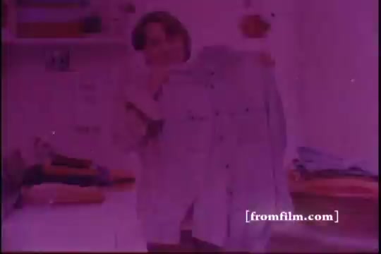 The still features a person holding up a light-colored shirt, showcasing its cleanliness. The room appears bright and slightly pinkish, indicative of aging film and lighting effects common in 1970s commercials. There are other items in the background, possibly laundry, suggesting a domestic setting focused on the effectiveness of Lestoil detergent. The overall mood conveys a sense of satisfaction and product endorsement.