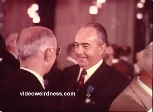 The still from the 1970s 'Blue Bonnet Margarine Commercial' features a gathering likely set at a formal event. Two men are engaged in conversation, with one appearing to smile warmly, possibly in a friendly exchange. The setting hints at a celebratory atmosphere, with soft lighting and an elegant backdrop. The use of 16mm film gives the image a vintage quality, capturing the essence of that era's advertising style.   For nostalgia and more content, follow on Twitter @FromFilm or like and subscribe on YouTube.