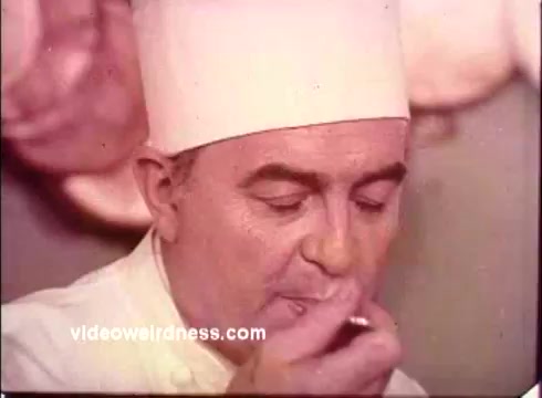 The still from the 1970s Blue Bonnet Margarine commercial features a man in a chef's hat, likely a culinary professional, tasting something from a small spoon. His focused expression suggests he is evaluating the flavor or quality of the margarine. The color palette and soft focus characteristic of 16mm film evoke a nostalgic feel, reflecting the advertising style of that era. Overall, the scene conveys an emphasis on the taste and quality of the product, aligning with the commercial's promotional intent.