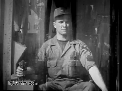 The still captures a soldier, likely James Daly, sitting in the cockpit of a CH-54 helicopter. He wears a military uniform and a cap, exuding a sense of confidence and responsibility. The background suggests the interior of a helicopter, highlighting the operational environment of the US Army during the Vietnam War. This image emphasizes the role of a flight engineer, showcasing the soldier's connection to the aircraft, which is depicted as a vital asset in transporting heavy equipment.