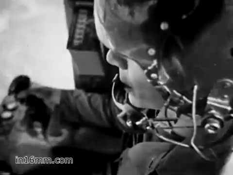 The still from 'Your Man in Vietnam' features a close-up of a U.S. Army specialist, likely James Daly, as he operates a CH-54 helicopter. The image captures the intensity of his role, showcasing his focus and the military equipment around him, emphasizing the demanding nature of his duties as a flight engineer. The film highlights the versatility of the CH-54, which he maneuvers to transport heavy machinery in challenging conditions.