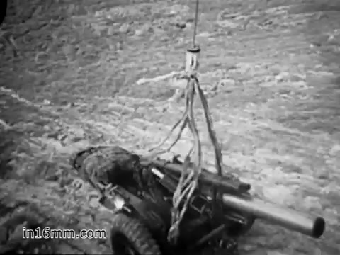 The still from 'Your Man in Vietnam,' featuring James Daly, likely depicts a CH-54 helicopter lifting a piece of artillery. The image illustrates the helicopter's capability to transport heavy military equipment, emphasizing the role of flight engineers like Daly in supporting operations. The scene captures the rugged terrain of Vietnam, highlighting the logistical challenges faced by the Army during the war. The imagery underscores the practical aspects of military aviation and the importance of such aircraft in the conflict.