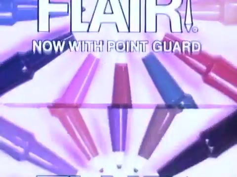 The still features a vibrant display of Flair pens arranged in a circular pattern, highlighting various colors. The text “FLAIR!” is prominently displayed at the top, with “NOW WITH POINT GUARD” below it. This emphasizes the product's durability and functionality. The overall aesthetic reflects a fun, playful 1970s style, typical for commercial graphics of that era. The color scheme is bright, drawing attention to the diverse range of pens.   Follow us on Twitter @FromFilm for more insights!