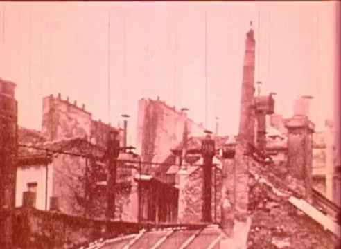 The still from 'Erik Satie and the King of the Beans - Part I' features a sepia-toned view of rooftops, characterized by chimneys and brick structures. The scene conveys a sense of an urban setting, reflecting historical architecture typical of the era. The image likely sets a backdrop for exploring Erik Satie's life and creative context in the film.