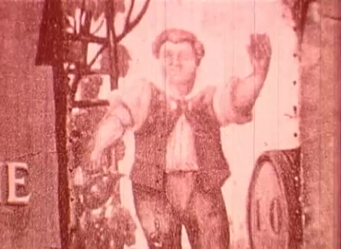 The still from 'Erik Satie and the King of the Beans - Part I' features a jovial, plump character with a rounded face and a friendly expression, dressed in period clothing that includes a vest and shirt. His arms are raised in a lively gesture, suggesting movement or celebration. The background hints at a rustic setting, possibly indicating an old-time harvest or festival scene. The overall tone is bright and whimsical, in keeping with the educational theme of the film.