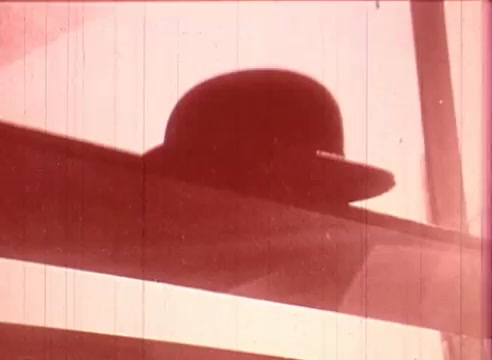 The still from 'Erik Satie and the King of the Beans - Part I' features a silhouette of a bowler hat against a soft, warm background. The image exhibits a vintage aesthetic typical of 16mm film, with visible scratches and grain. The composition suggests a sense of whimsy or intrigue, aligning with the educational theme of the film.
