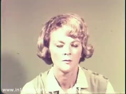 The still features a woman with blonde, wavy hair, appearing serious and contemplative. She is seated against a plain background, dressed in a light-colored top. This moment likely emphasizes the emotional impact of the message about measles and its potential connection to mental disability, reflecting the tone of public health awareness in the 1968 PSA. The 16mm print quality gives it a vintage look, characteristic of that era's informational films.