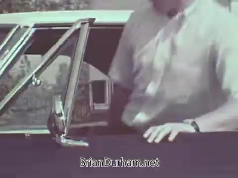 The 16mm still from the 'Automotive Safety Foundation PSA - 1960s' shows a man interacting with a car, likely demonstrating safety features or practices. The focus appears to be on automobile safety awareness, as typical in public service announcements from that era. The visual elements suggest a suburban or outdoor setting, emphasizing the relevance of automotive safety in everyday life.