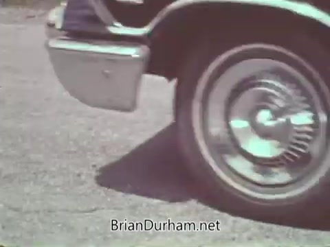 The still from the 'Automotive Safety Foundation PSA - 1960s' features a close-up of a car's wheel and tire on a paved surface. The focus emphasizes the wheel's design and movement, likely illustrating aspects of automotive safety, such as tire performance or stability. The overall look is characteristic of the 1960s, with a vintage color palette.