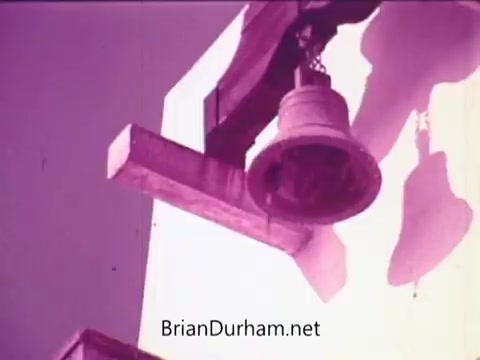 The still from the 'Pepsi commercial - Todos junto a Pepsi siempre libre y feliz' features a close-up view of a bell hanging on a wooden structure against a bright background. The color palette has a vintage feel, with a predominance of purples and whites, suggesting a nostalgic or celebratory tone. The imagery emphasizes themes of community and happiness, aligning with the commercial's message.