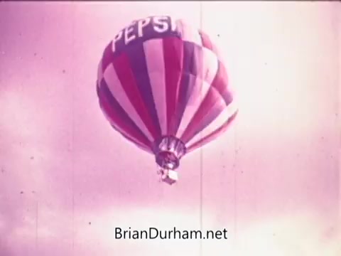 The still features a colorful hot air balloon branded with the Pepsi logo, soaring against a slightly cloudy backdrop. The color scheme includes red, white, and blue stripes, emphasizing the brand's identity. This image captures a sense of freedom and joy associated with the Pepsi brand.