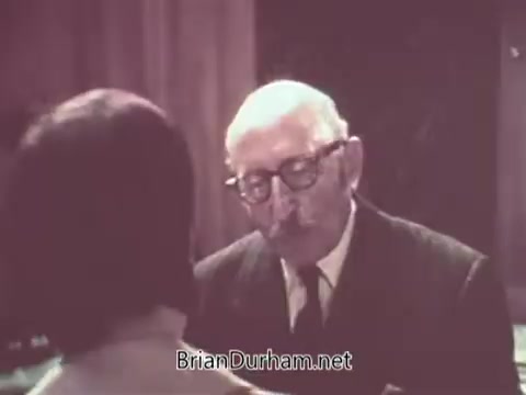 The still features an older man wearing glasses engaged in conversation, likely with a younger individual out of frame. The setting appears to reflect a personal or intimate environment, suggesting a casual or familial interaction. The color tone and style indicate it originates from the 1970s, aligning with the era's aesthetics. The context relates to Nabisco's marketing, possibly promoting their Escort Crackers.