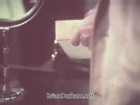 The still features a close-up of a hand holding a box of Nabisco Escort Crackers, likely from a 1970s advertisement. A reflective surface, possibly a mirror, is visible in the background, hinting at a setting focused on presentation and indulgence. The overall scene conveys a sense of nostalgia and classic marketing aesthetics from that era.