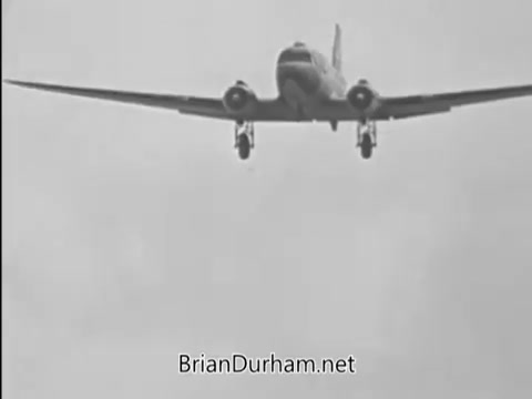 The still features a low-flying aircraft, likely a vintage propeller plane, set against a cloudy sky. This image is part of a public service announcement from the Vietnam era, emphasizing the promotion of buying bonds. The visual captures a sense of urgency and support for the military effort during that time.