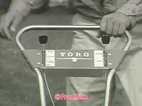 The still features a close-up of a Toro Whirlwind Lawnmower's handle, highlighting the brand name 'TORO' prominently displayed on the mower. A person's hand grips the handle, suggesting use of the machine, set against a blurred background that implies a grassy area. The overall presentation evokes a vintage aesthetic typical of 1960s advertisements, emphasizing simplicity and functionality.