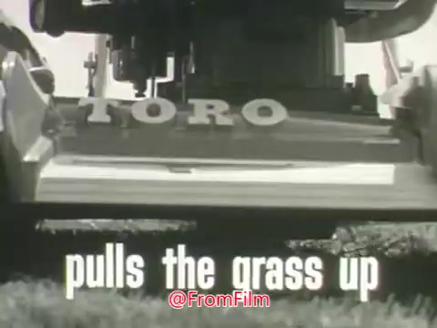 The still depicts a close-up of the Toro Whirlwind Lawnmower, focusing on its blade and grass-cutting mechanism. The word 'TORO' prominently appears on the machine, while the phrase 'pulls the grass up' is featured in bold text below. The black-and-white image captures the vintage aesthetic typical of 1960s commercials, emphasizing the lawnmower's functionality.