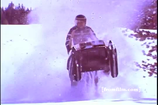 The still from the Ski-doo snowmobile commercial showcases a snowmobile in action, kicking up a spray of powdery snow. The rider, dressed in winter gear and a helmet, appears to be performing a jump or a stunt, emphasizing the excitement and thrill of winter sports associated with Ski-doo. The snowy landscape in the background reinforces the adventurous spirit of snowmobiling, characteristic of the 1970s era. The imagery effectively captures the exhilaration of the sport and promotes the Ski-doo brand.