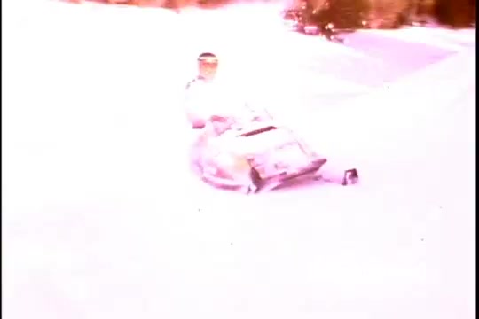 The 16mm still from the 1970s Ski-Doo snowmobile commercial depicts a snowmobiler navigating through a snowy landscape. The snowmobile is prominently featured, showcasing its design and capabilities. The rider appears to be enjoying the experience, emphasizing the thrill of winter sports. The bright, slightly faded coloring characteristic of vintage film adds a nostalgic touch, reflecting the era's outdoor adventure spirit. Overall, it captures the excitement and freedom associated with Ski-Doo's brand in the winter sports scene.
