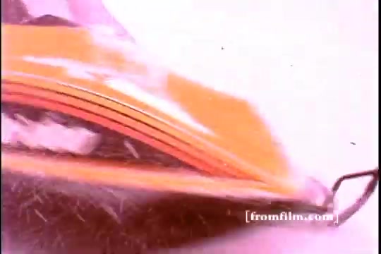 The still from the 1970s Ski-Doo snowmobile commercial showcases a close-up view of the snowmobile’s sleek design and vibrant colors, particularly highlighting its orange and black features. The shot captures snow being kicked up by the snowmobile, emphasizing its speed and agility on winter terrain. The snowy background suggests a cold, exhilarating environment, characteristic of winter sports. This imagery encapsulates the excitement and outdoor adventure associated with Ski-Doo snowmobiles.