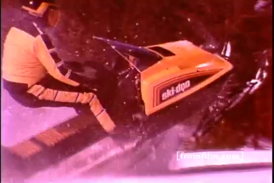 The still depicts a person riding a Ski-Doo snowmobile, showcasing the iconic design and bright yellow color of the machine. The rider is dressed in a winter sports outfit, emphasizing the activity's adventurous nature. The background suggests a snowy environment, typical for skiing and snowmobiling, highlighting the winter sports theme of the commercial.