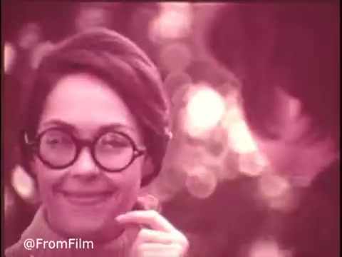 The still from the 1970s Colgate Pruf Spray Starch features a smiling woman wearing round glasses and a light-colored top, seemingly engaged in conversation. The background has a soft, dreamy blur, characteristic of the era's cinematography. The warm tones and nostalgic ambiance reflect the marketing style of that period. Follow us on Twitter @FromFilm for more vintage gems!