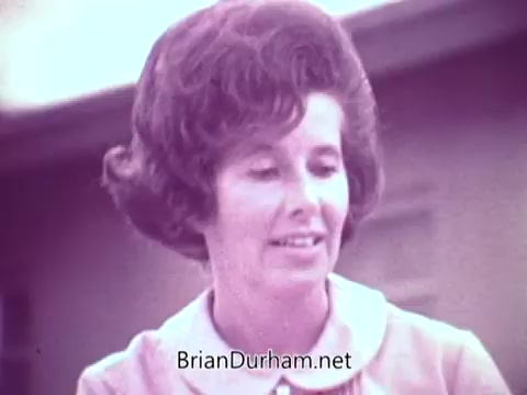 The still from the 'Cold Power Detergent' commercial features a woman with a prominent, styled hairstyle, wearing a collared shirt. She appears to be engaging and smiling, possibly presenting or discussing the product. The background suggests a casual, sunny environment typical of Florida, enhancing the commercial's inviting tone.