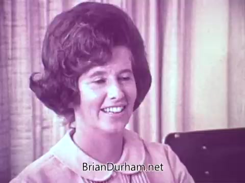 The still features a woman with a voluminous hairstyle, smiling warmly while seated in front of a backdrop of curtains. She appears engaged and friendly, suggesting a positive mood, likely to promote Cold Power Detergent in the commercial set in Ft. Myers, Florida. The colors are likely soft and pastel, typical for advertisements of that era.