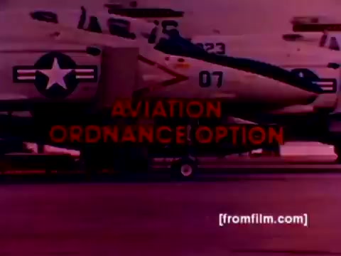 The still from the 'USMC Aviation Ordnance enlistment film' showcases a lineup of military aircraft, including F-4 Phantoms, AH-1 SuperCobras, an FA-18, and a Harrier. The image prominently displays the phrase 'AVIATION ORDNANCE OPTION' in bold red text, emphasizing the focus on ordnance enlistment. The aircraft are set against a backdrop that appears to have a purplish hue, likely due to the 16mm film's color quality. The scene likely depicts ordnance being mounted, featuring missiles and bombs, capturing the essence of the Marine Corps' technical roles in aviation.