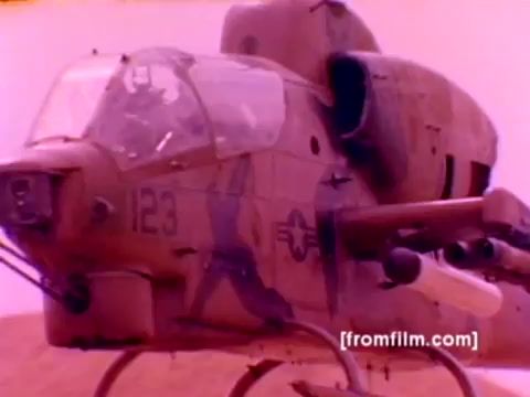 The still from the 'USMC Aviation Ordnance enlistment film' depicts an AH-1 SuperCobra helicopter preparing for ordnance mounting. The aircraft is shown in a dynamic pose, emphasizing its military capabilities. Surrounding it are scenes of F-4 Phantoms, FA-18s, and Harriers, highlighting various Marine Corps aircraft involved in ordnance operations. The visual elements, including the ordnance such as missiles and bombs being mounted, showcase the technical and operational aspects of aviation ordnance within the Marine Corps. The color correction aims to enhance the image clarity and vibrancy, providing a more accurate representation of the aircraft and equipment.