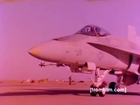 The still from the 'USMC Aviation Ordnance enlistment film' features an FA-18 aircraft prominently displayed on a runway. Surrounding it may be additional military hardware, including F-4 Phantoms, AH-1 SuperCobras, and Harriers, showcasing the diverse capabilities of Marine Corps aviation. The image captures ordnance being mounted, highlighting missiles and bombs integral to the aircraft's functionality. The color correction enhances the visibility of details and technology, providing a clearer representation of the aircraft in a military setting. Overall, the scene emphasizes the importance of ordnance in Marine aviation operations.
