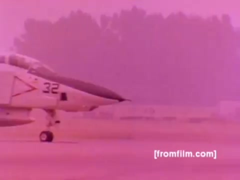 The 16mm still from the 'USMC Aviation Ordnance enlistment film' showcases a dramatic scene featuring military aircraft, specifically an F-4 Phantom jet prominently displayed. The background hints at a military setting with blurred activity, typical of an airfield.  In the film, various Marine Corps aircraft, including AH-1 SuperCobras, FA-18s, and Harriers, are highlighted in the context of ordnance operations, focusing on the mounting of missiles and bombs. The color correction process aims to enhance the hues, shifting away from the overwhelming pink tone to more realistic colors to better represent the aircraft and environment.   The overall imagery emphasizes the technical aspects of aviation ordnance and the dynamics of military enlistment options in the Marine