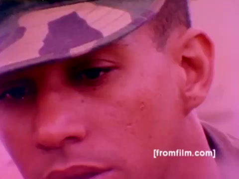 The still from the 'USMC Aviation Ordnance enlistment film' captures a close-up of a Marine in uniform, focusing intently, likely during an instructional moment. The background likely hints at aviation equipment or ordnance-related tasks. The color correction enhances the image, bringing out more natural skin tones and details in the fabric of the uniform while maintaining the military context of the film, which showcases various aircraft like F-4 Phantoms, AH-1 SuperCobras, FA-18s, and Harriers, alongside ordnance being mounted. The overall tone reflects a serious and focused environment essential for the ordnance field within the Marine Corps.